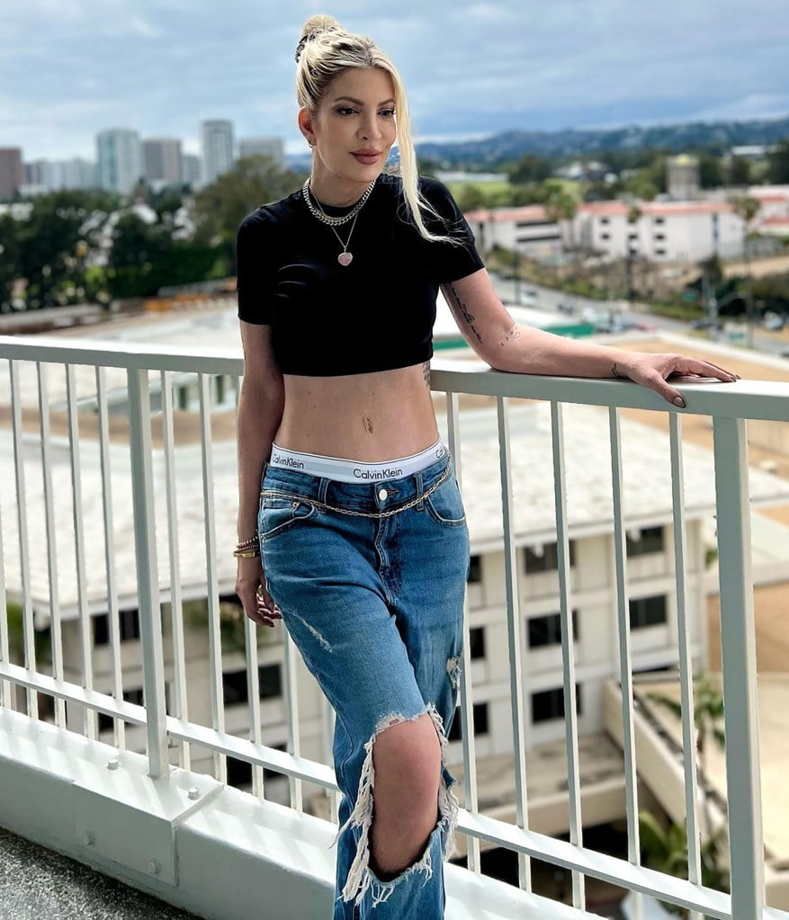 tori spelling on a blacony wearing a crop top and ripped jeans