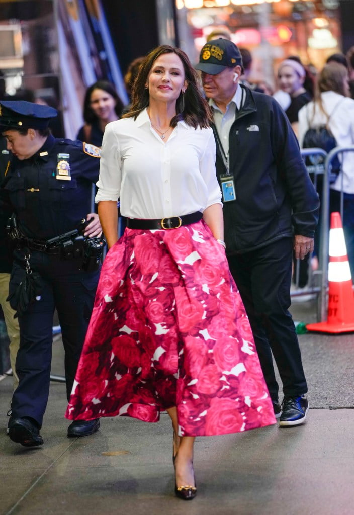 Jennifer Garner smiles in a pink floral midi skirt worn with a white button-down blouse, black belt, and black heels